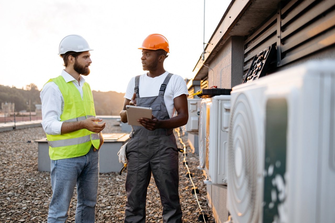 Two HVAC professionals reviewing a tablet beside rooftop air-conditioning units