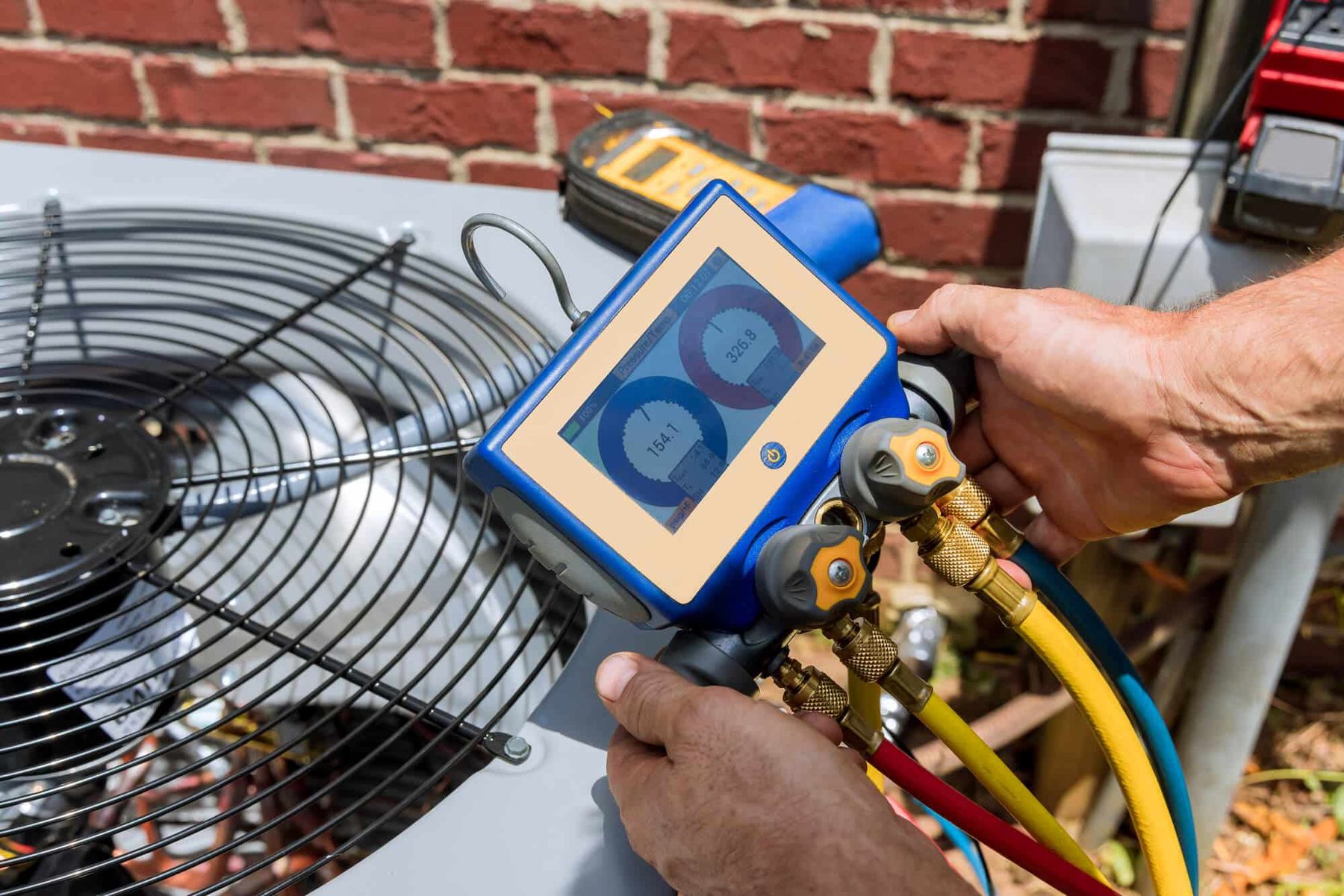 Technician checking an HVAC condenser with a manifold pressure gauge