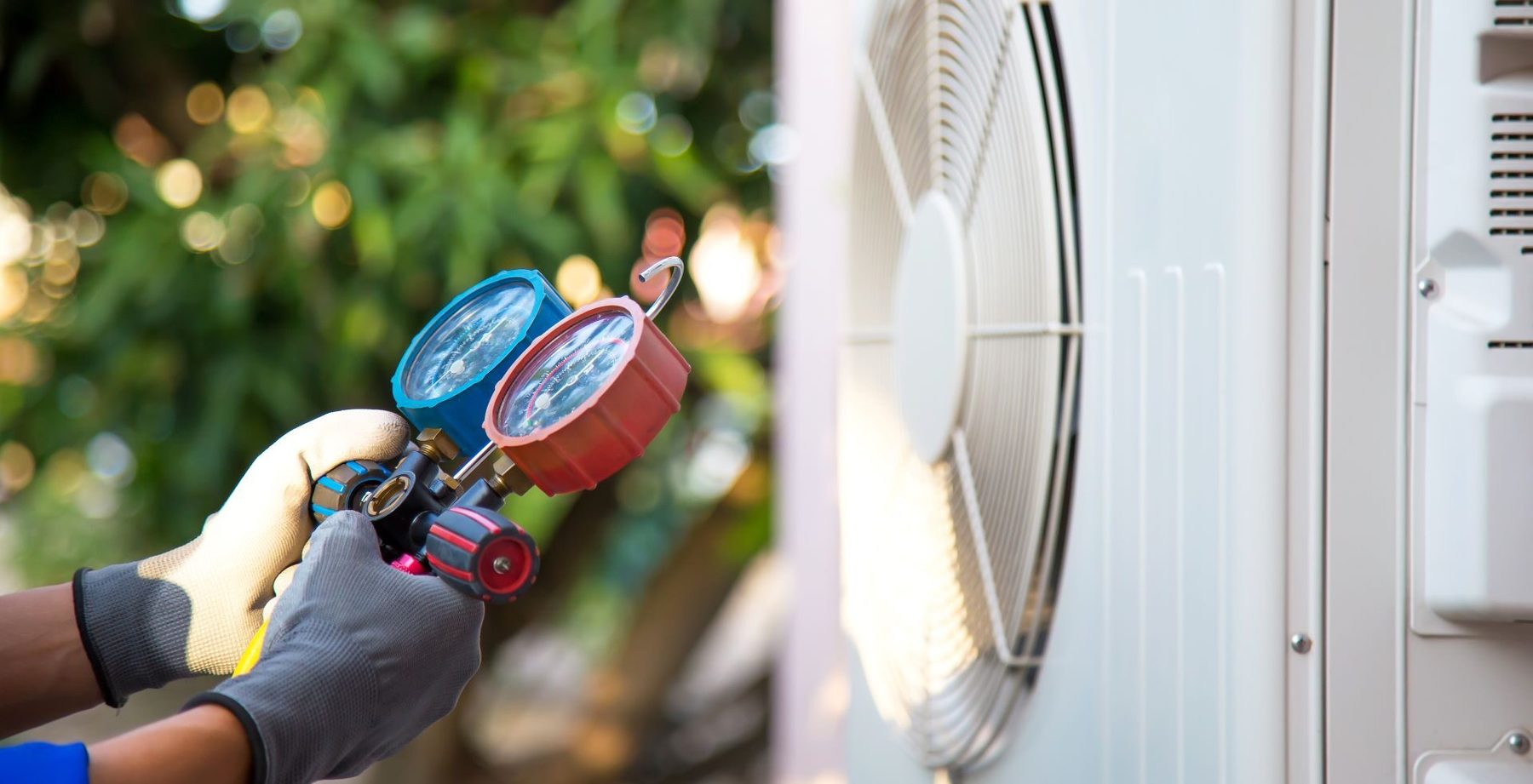 Technician checking an outdoor AC condenser with a manifold gauge set