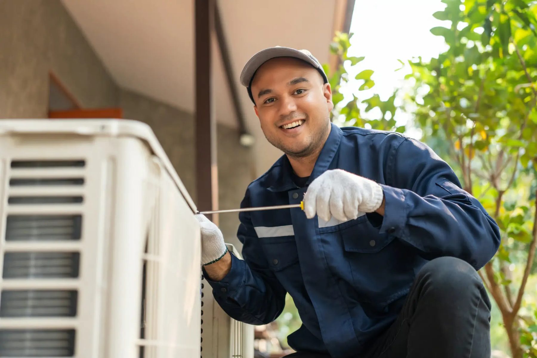 HVAC technician servicing an outdoor air-conditioning unit with a screwdriver